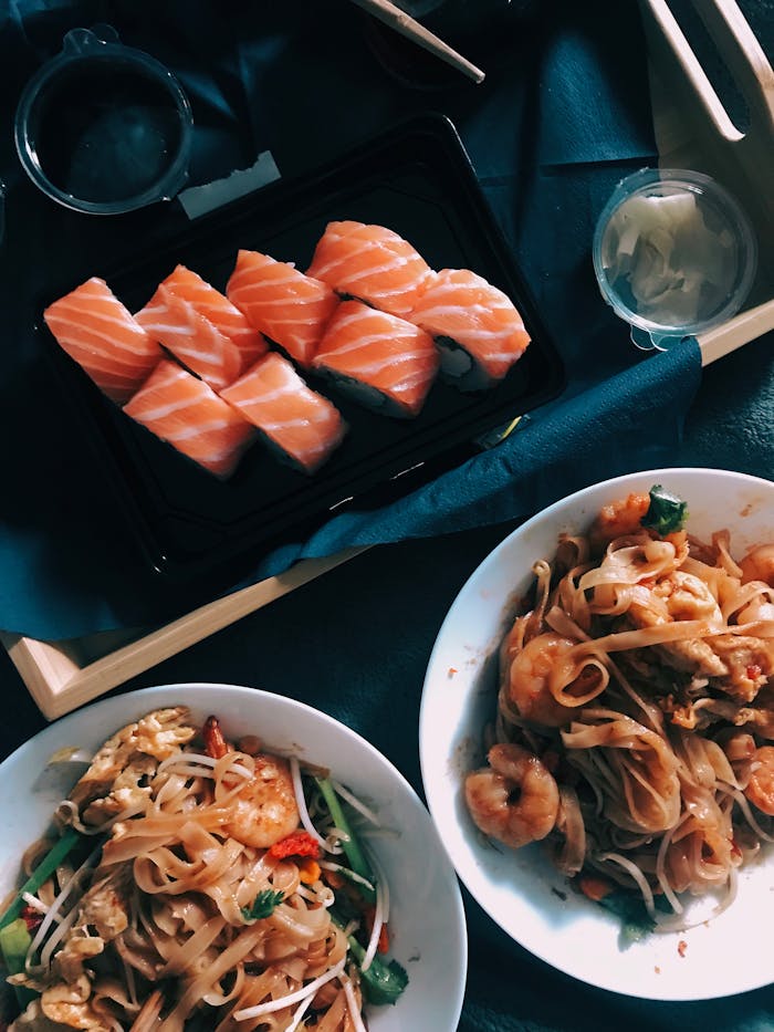Top view of sushi and noodle dishes on wooden tray, perfect for food lovers.